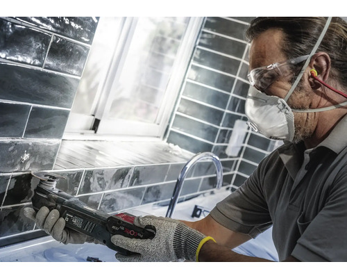 Handwerker arbeitet mit einem Multifunktionswerkzeug an Fliesen in einem Badezimmer