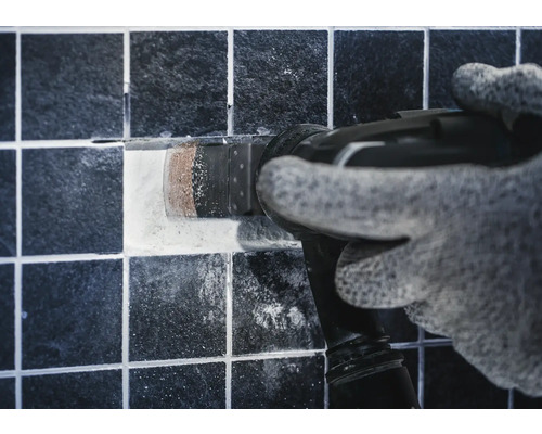 Artisan retirant un carreau avec un outil multifonction.