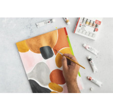 Une personne peint un tableau abstrait avec des couleurs acryliques. Des tubes de peinture et des pinceaux sont à portée de main.