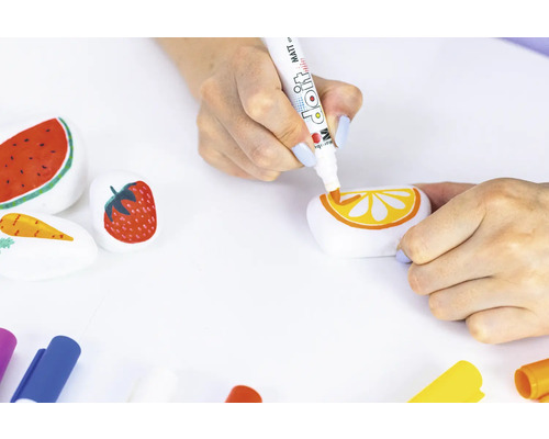 Une personne peint des motifs de pastèque, de fraise, de carotte et d''orange sur des pierres à l''aide d''un feutre de couleur.