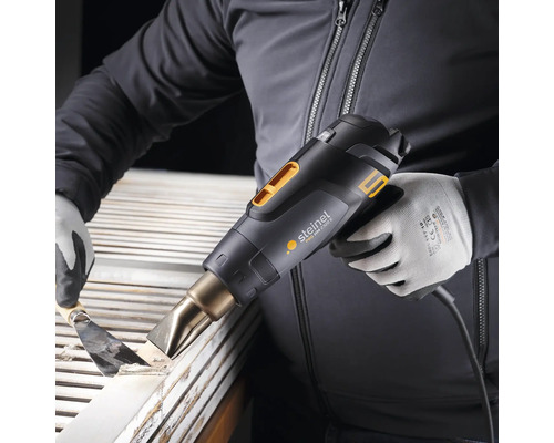 Eine Person entfernt mit einer Heißluftpistole Farbe von Holz.