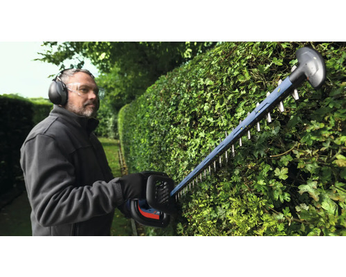 Un homme taille une haie avec un taille-haie et porte un équipement de protection.