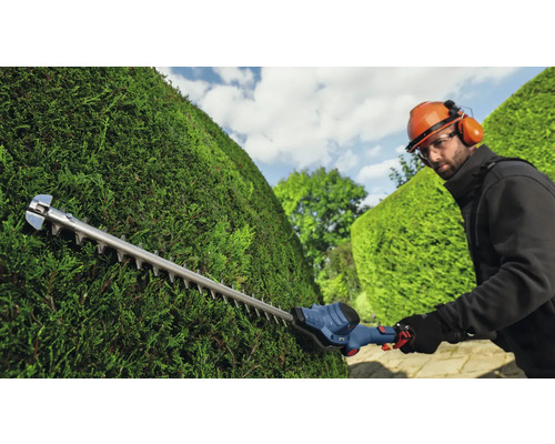 Une personne taille une haie avec un taille-haie.
