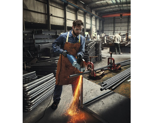 Un homme dans un atelier coupe un tuyau métallique avec une meuleuse d''angle, avec des étincelles.