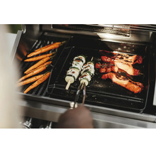 Gemüse wie Karotten, Zucchini-Spieße und Tomaten werden auf einem Grill zubereitet.