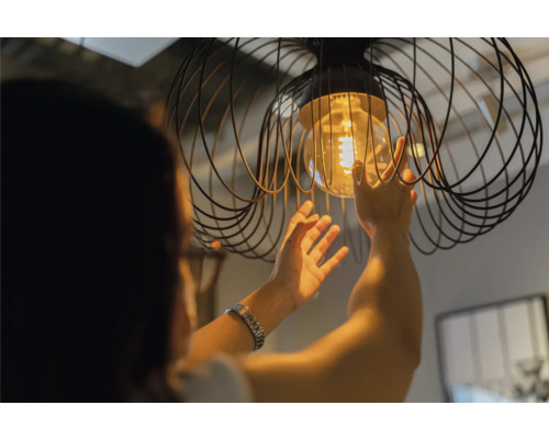 Une personne remplace une ampoule dans une suspension avec une cage métallique.