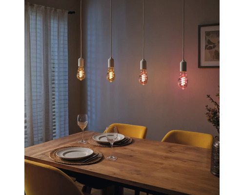 Table à manger avec quatre ampoules suspendues émettant différentes couleurs de lumière.