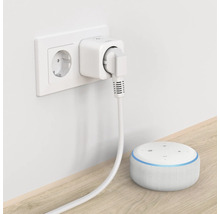 Intelligente Steckdose mit eingestecktem Stecker in einer Wandsteckdose und ein intelligenter Lautsprecher auf einer Oberfläche