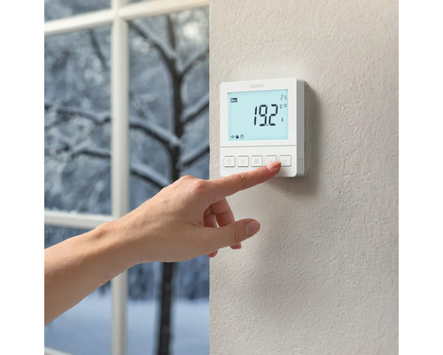 Une main actionne un thermostat Hama au mur.