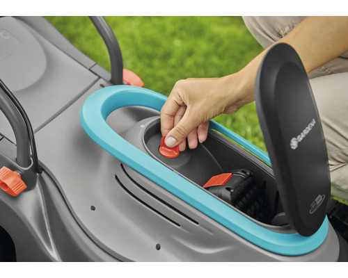 Eine Hand setzt einen roten Knopf in einen Rasenmäher mit geöffnetem Batteriefach. Gardena Logo sichtbar.