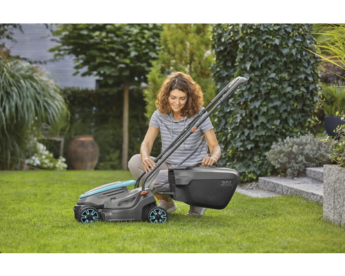 Eine Frau hockt im Garten und montiert einen Rasenmäher mit einem 30 Liter Fangkorb.