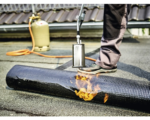 Couvreur soudant une membrane bitumineuse avec un brûleur et une bouteille de gaz.