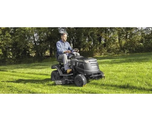 Ein Mann fährt einen Rasentraktor auf einer Wiese.