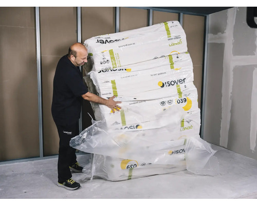 Un homme manipule une pile de paquets de laine d''isolation Isover sur un chantier.