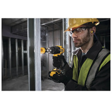 Ein Mann bohrt mit einer Bohrmaschine ein Loch in eine Metallwand. Er trägt eine Schutzbrille, einen Helm und Ohrstöpsel.