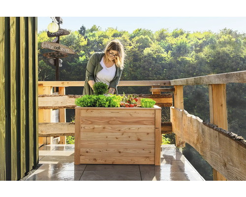 Une femme plante de la salade et des légumes dans un potager surélevé en bois sur une terrasse.