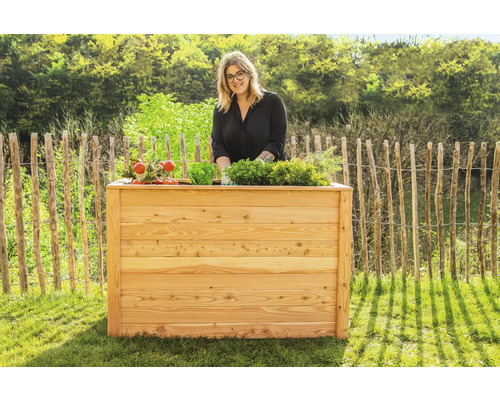 Femme se tient derrière un potager surélevé en bois avec divers légumes dans le jardin
