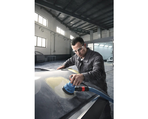 Un homme ponce un capot de voiture avec une ponceuse excentrique dans un atelier.
