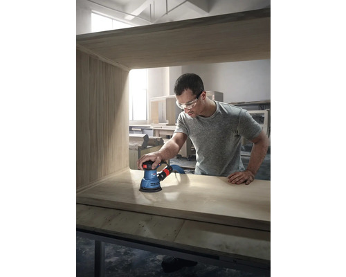 Un homme ponce un meuble en bois avec une ponceuse excentrique de la marque Bosch.