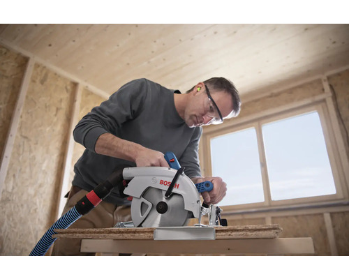 Un homme scie une planche de bois avec une scie circulaire Bosch dans un bâtiment brut.