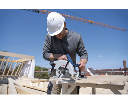 Un artisan portant un casque de protection est en train de scier du bois avec une scie circulaire Bosch sur un chantier.