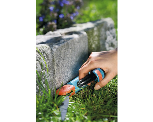 Eine Person verwendet eine Rasenkantenschere zum Schneiden von Gras entlang einer Steinmauer.