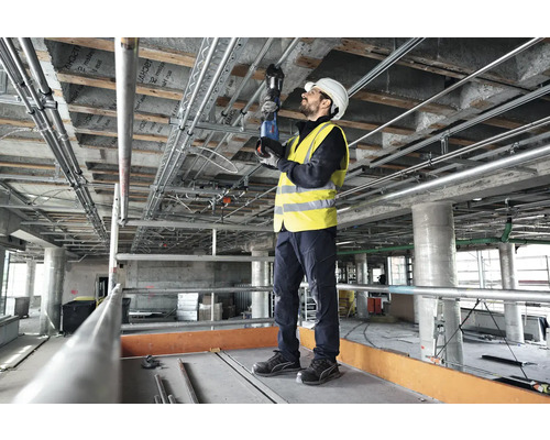 Un ouvrier monte des tuyaux au plafond d'un bâtiment brut à l'aide d'une clé à tube.