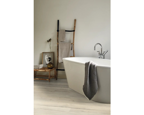 Helles Badezimmer mit freistehender Badewanne, Handtüchern auf einer Holzleiter und einer Holzbank mit Dekorationen