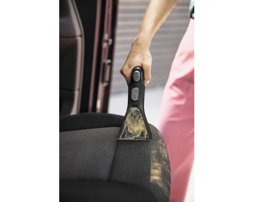 Gros plan d''une personne nettoyant un siège de voiture avec un détachant portable.