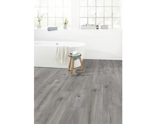 Helles Badezimmer mit Badewanne, Hocker und grauem Laminatboden.