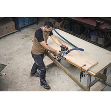 Un homme travaille avec une défonceuse sur une pièce sur un établi dans un atelier.