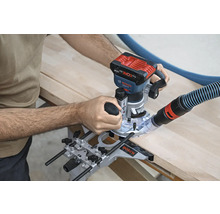 Une défonceuse est utilisée pour travailler une pièce de bois. Un tuyau d'aspirateur est fixé à la machine.