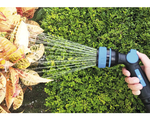 Eine Hand hält einen Gartenschlauch, der Pflanzen bewässert.