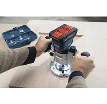 Une personne utilise une défonceuse à batterie Bosch sur une planche de bois, avec une boîte à outils bleue en arrière-plan.