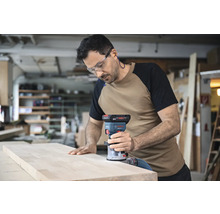 Un homme utilise une défonceuse sur une planche de bois dans un atelier.