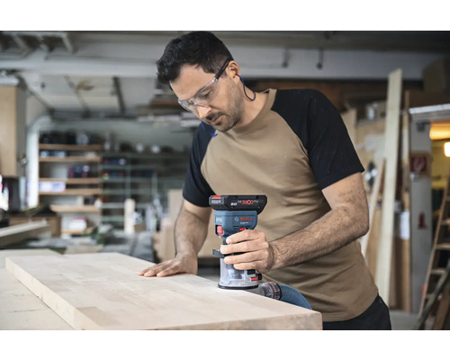 Un homme utilise une défonceuse sur une planche de bois dans un atelier.