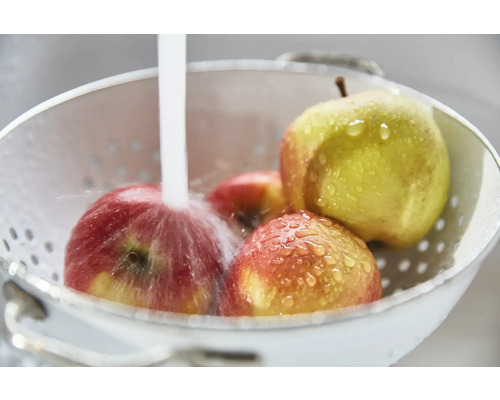 Des pommes sont lavées dans une passoire blanche sous l''eau courante