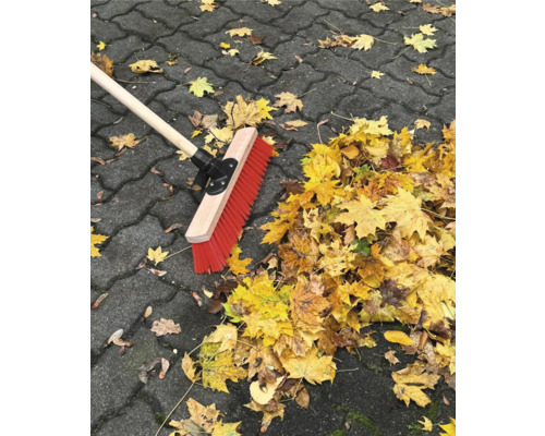 Kehrbesen mit Holzstiel und Herbstlaub auf Pflastersteinen