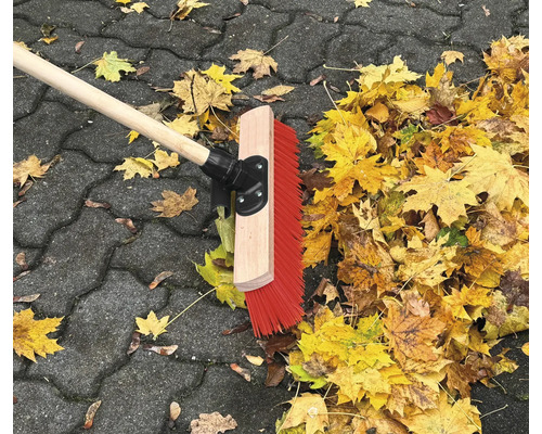 Strassenbesen mit Holzstiel und Herbstlaub auf Pflastersteinen