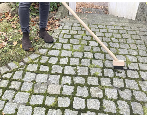 Person reinigt Steinpflaster mit Fugenbürste