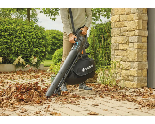 Une personne utilise un aspirateur souffleur sans fil Gardena dans le jardin pour ramasser les feuilles.