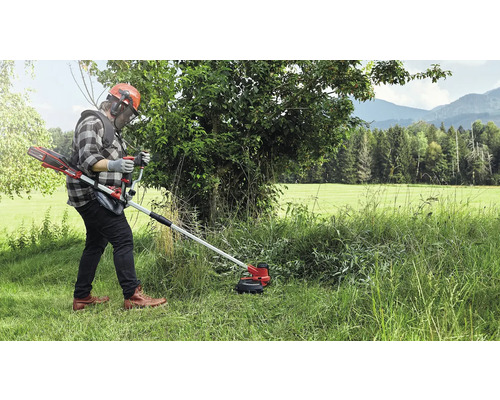 Une personne utilisant un coupe-bordures à batterie dans un environnement extérieur herbeux.