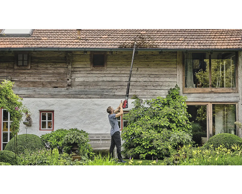 Mann reinigt Dachrinne mit einem Dachrinnenreiniger vor einem Haus.