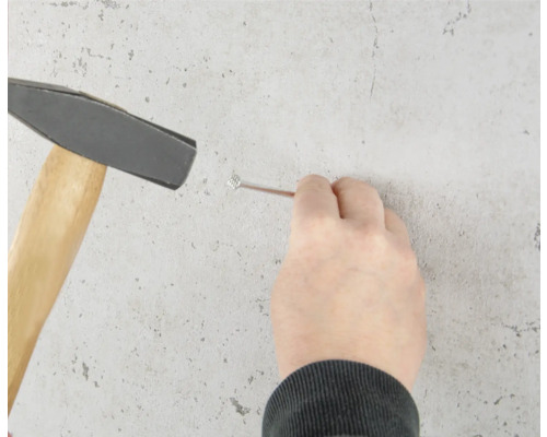 Eine Person schlägt mit einem Hammer einen Nagel in die Wand.