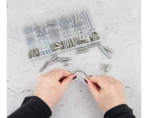 Sortiment verschiedener Zugfedern in einer transparenten Kunststoffbox, eine Feder wird von zwei Händen gehalten