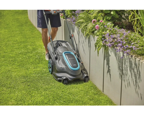 Ein Mann mäht mit einem Rasenmäher den Rasen entlang einer erhöhten Blumenrabatte