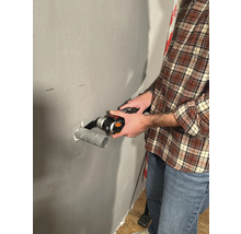 Un homme coupe un tuyau avec un outil multifonctionnel sur un mur.