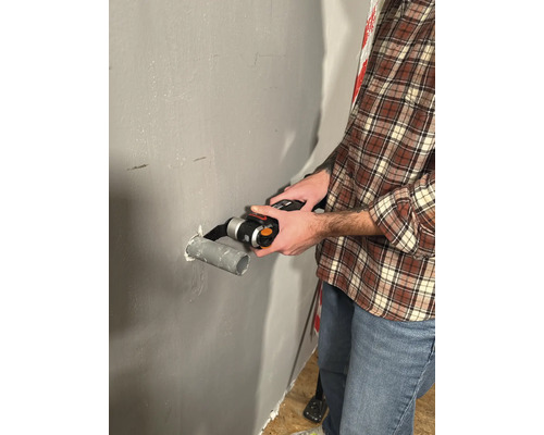 Un homme coupe un tuyau avec un outil multifonctionnel sur un mur.