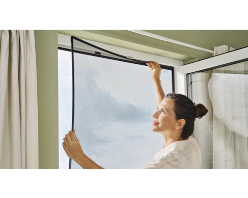 Femme installant une moustiquaire sur une fenêtre