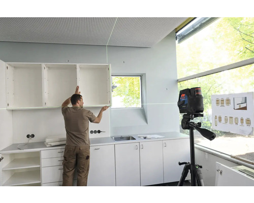 Un homme installe un élément haut à l''aide d''un laser lignes croisées dans une cuisine.